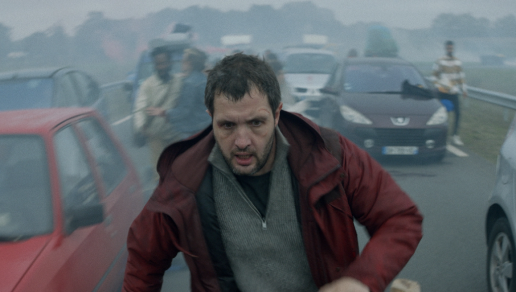 Vincent Must Die film still. A man runs amidst cars, looking distressed. Cannes '23 film review.