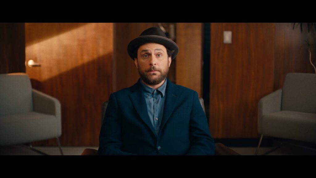 Charlie Day in Fool's Paradise movie. Actor wearing a hat and a blue suit. Comedy film scene.