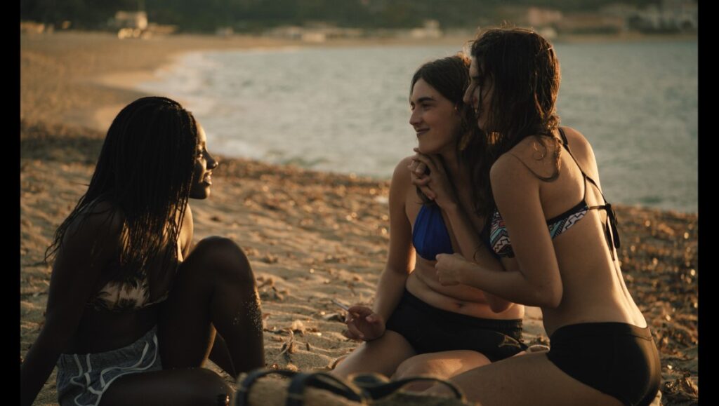 Homecoming movie scene: Three women in swimwear sit on a beach, conversing. Cannes '23 film review.