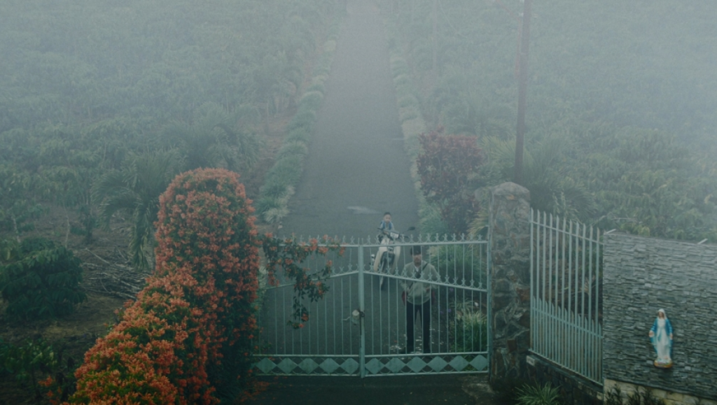 Inside the Yellow Cocoon Shell film scene. Foggy gate, motorcycle, statue. Phạm Thiên Ân movie review.