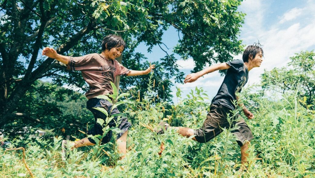 Two boys run through tall grass in Monster by Hirokazu Kore-eda.