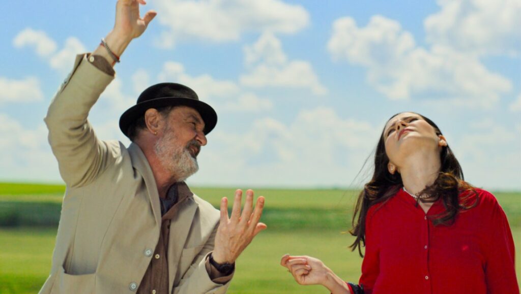 The Potemkinists — Radu Jude The Potemkinists movie still. Man in hat gestures, woman looks up to sky. Radu Jude film.