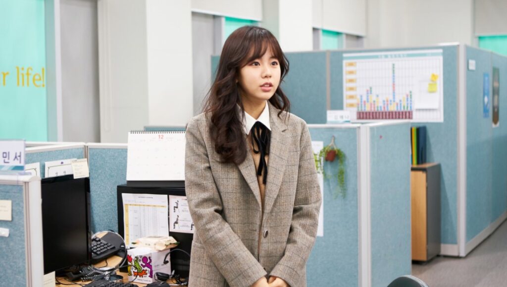Hong Sung-eun in Aloners film. Young woman in office setting, wearing a blazer and bow tie. Korean cinema.
