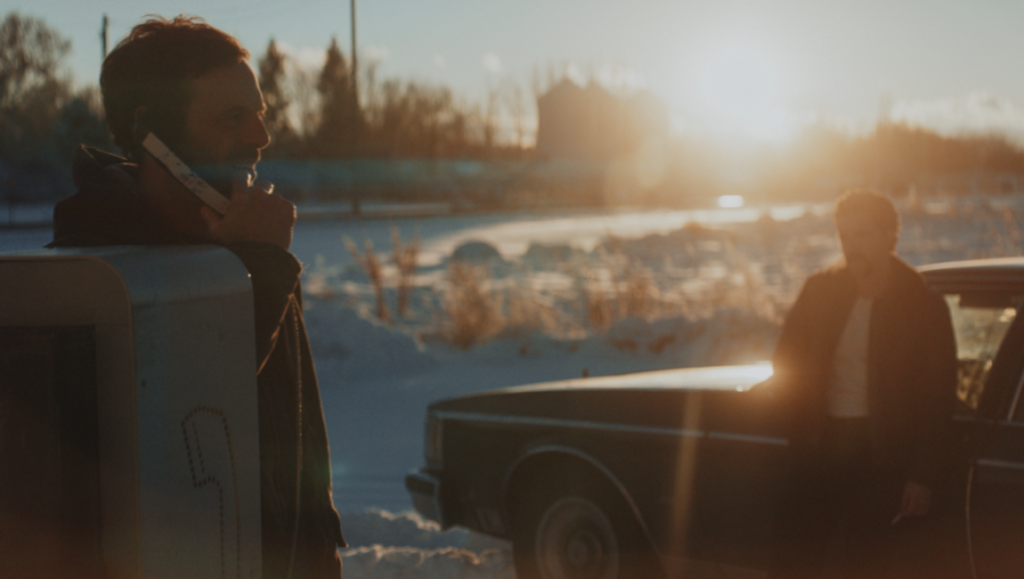 Blood for Dust film scene: Man on phone by car in snowy landscape at sunset.