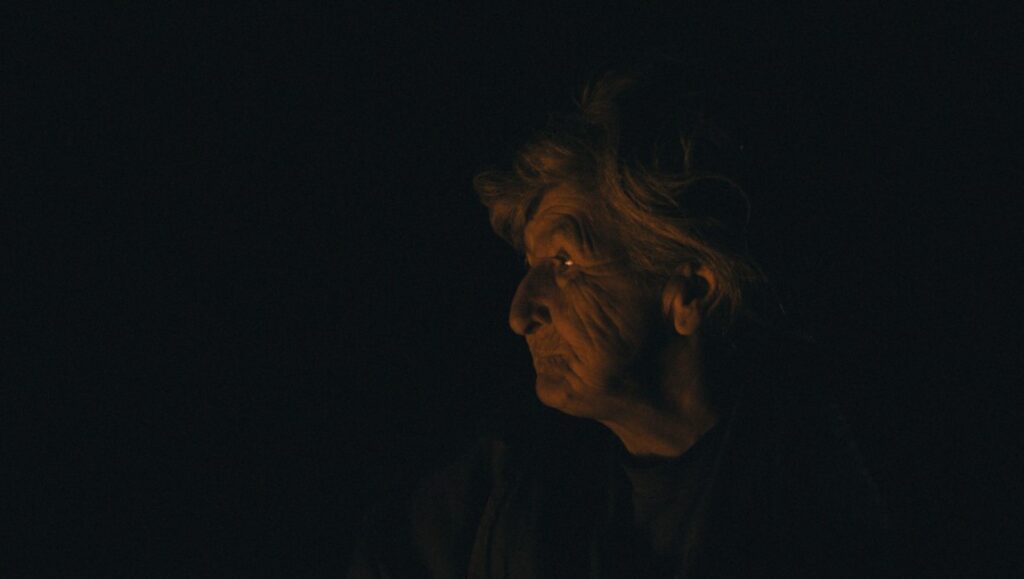 Profile of an elderly woman in the Museum of the Revolution, by Srdjan Keca. Dark, moody lighting.