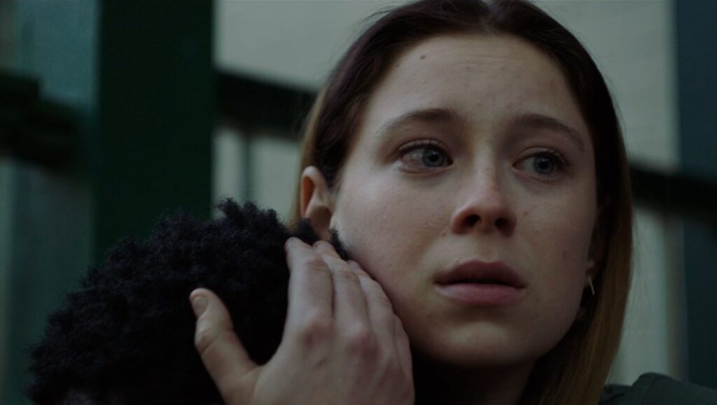 Mina Sundwall in The Graduates. Close-up of actress with hand near face, looking off-camera. Movie still.