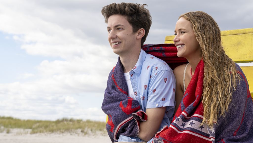 No Hard Feelings movie scene: Jennifer Lawrence and Andrew Barth Feldman on a beach, wrapped in blankets.