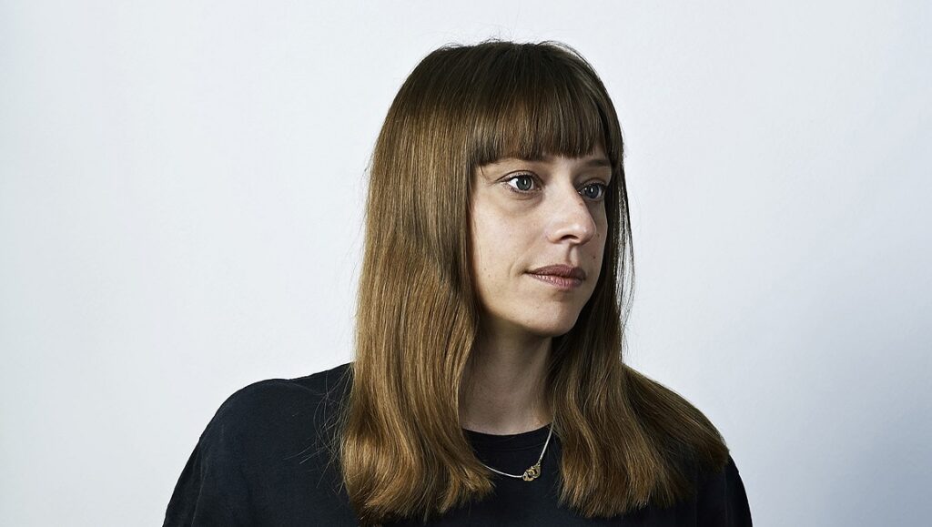 The Sound Before the Image: An Interview with Alice Winocour Alice Winocour, director of Revoir Paris, portrait. Woman with bangs, long brown hair, wearing a black shirt and necklace.