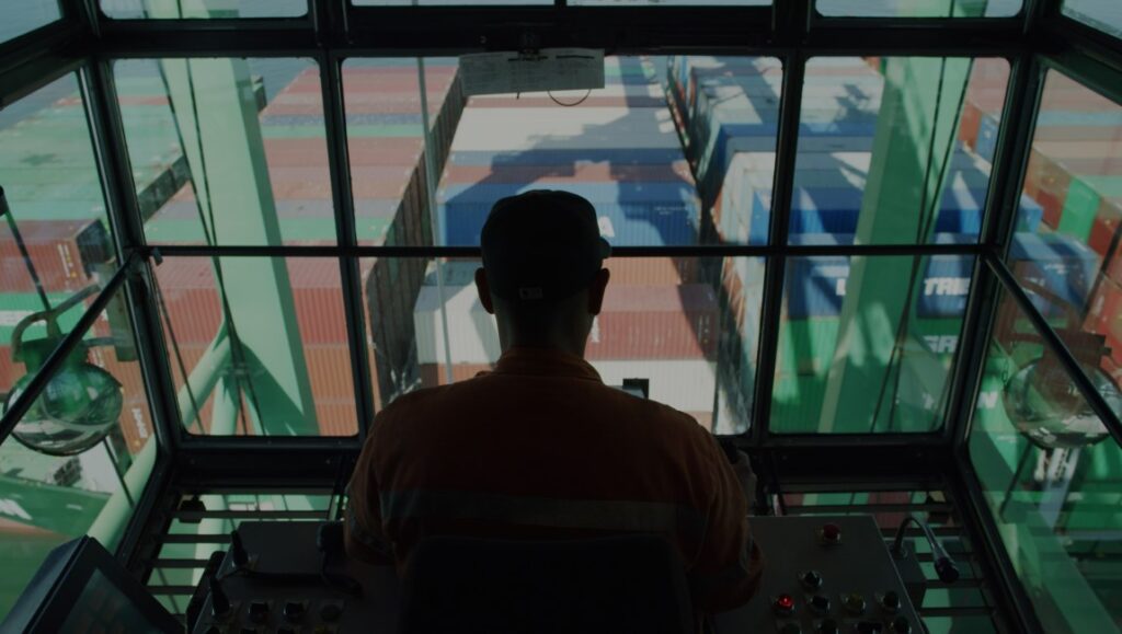 Users — Natalia Almada USERS film still. Man operating a crane overlooking shipping containers. Natalia Almada film.
