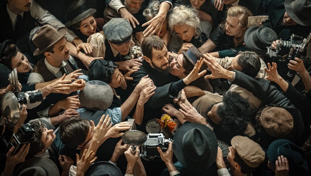 L'Abbé Pierre mobbed by fans. Cannes '23 review of Frédéric Tellier's A Century of Devotion film. Crowd scene with vintage cameras.