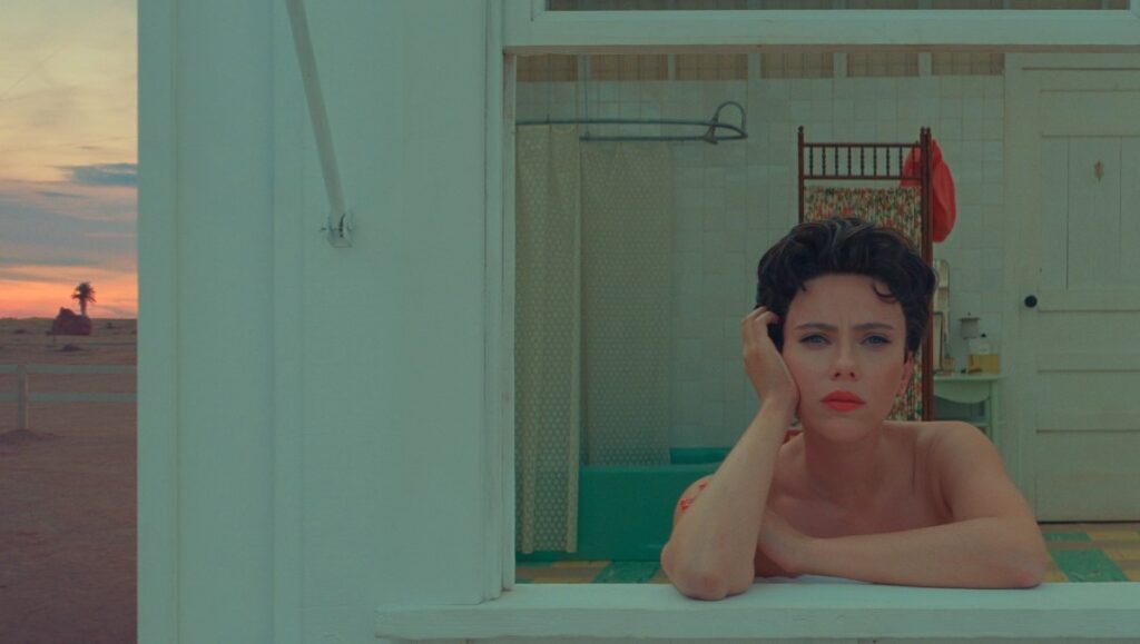 Scarlett Johansson in Asteroid City. Film still of actress looking out window, desert scene in background. Wes Anderson movie.
