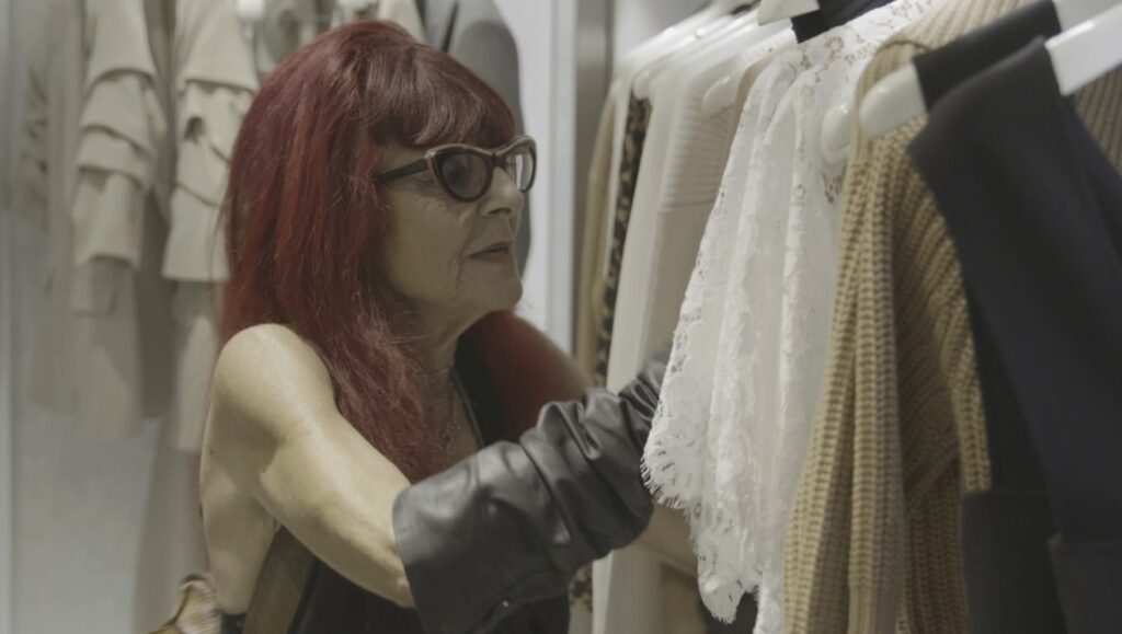 Woman with red hair shops for clothes. Rack of dresses and tops. Fashion boutique.