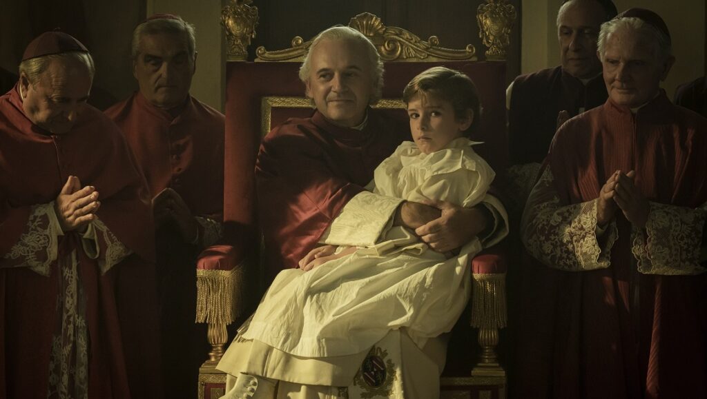 Kidnapped: The Abduction of Edgardo Mortara film scene. Pope Pius IX holds Edgardo, surrounded by cardinals.