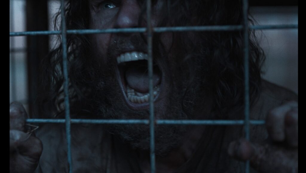 The Seeding movie still: Man with beard screams behind bars. Tribeca '23 film review.