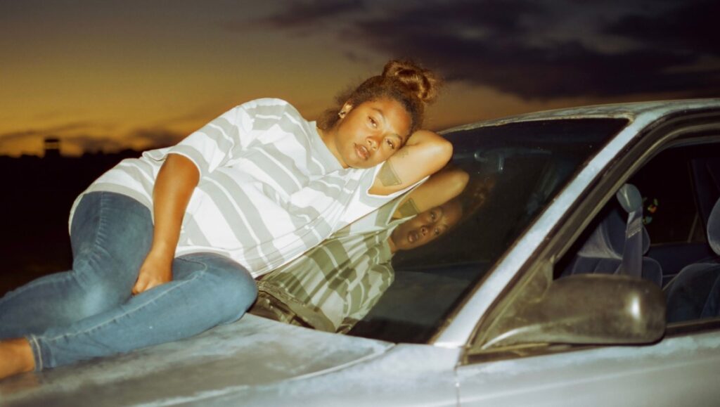 Earth Mama — Savannah Leaf Woman lying on a car windshield at sunset. Earth Mama movie still.
