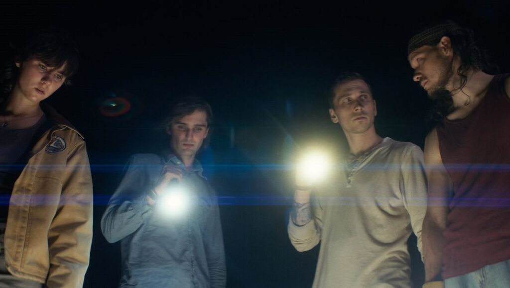 The Human Surge 3 film still from Locarno Film Festival 2023. Four young men hold flashlights in the dark.