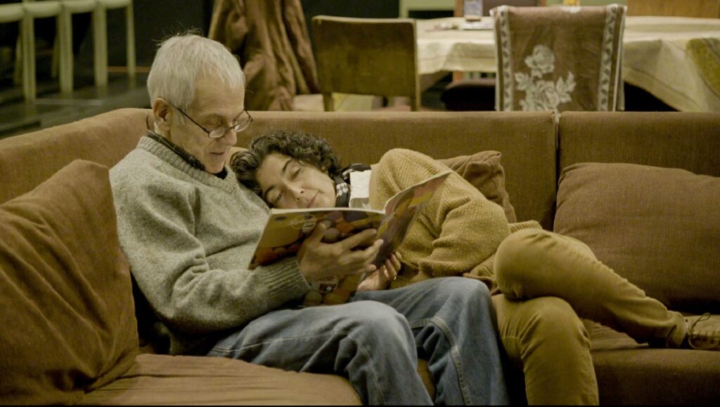 The Eternal Memory — Maite Alberdi The Eternal Memory film still. Couple reading on couch. Alzheimer's documentary. Maite Alberdi film.