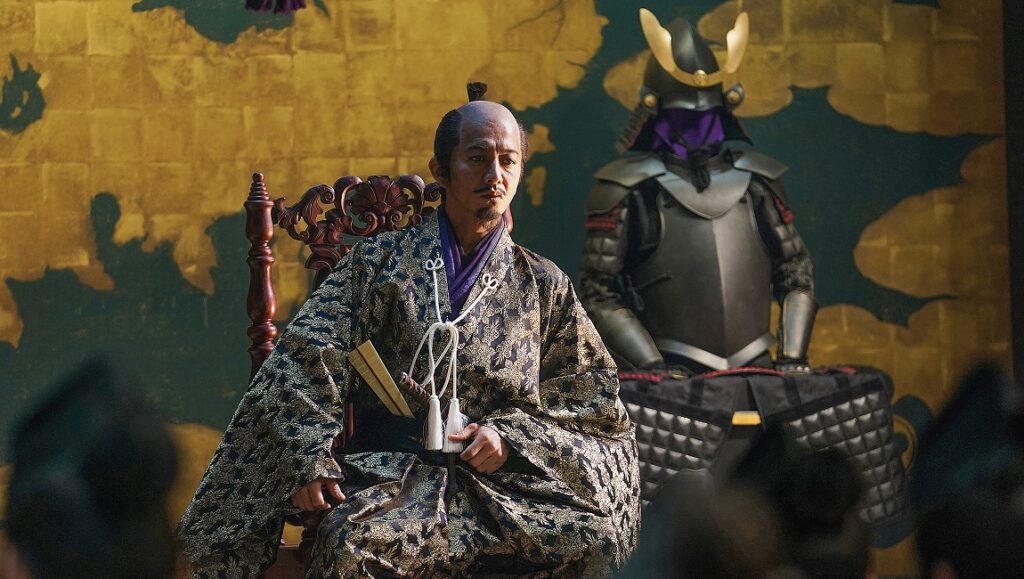 Japanese samurai lord in traditional clothing with armor in background. Historical drama.
