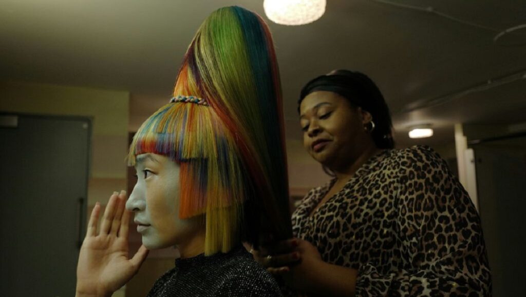 Medusa Deluxe — Thomas Hardiman Medusa Deluxe film still: Woman with rainbow hair getting styled. A24 movie, Thomas Hardiman film.