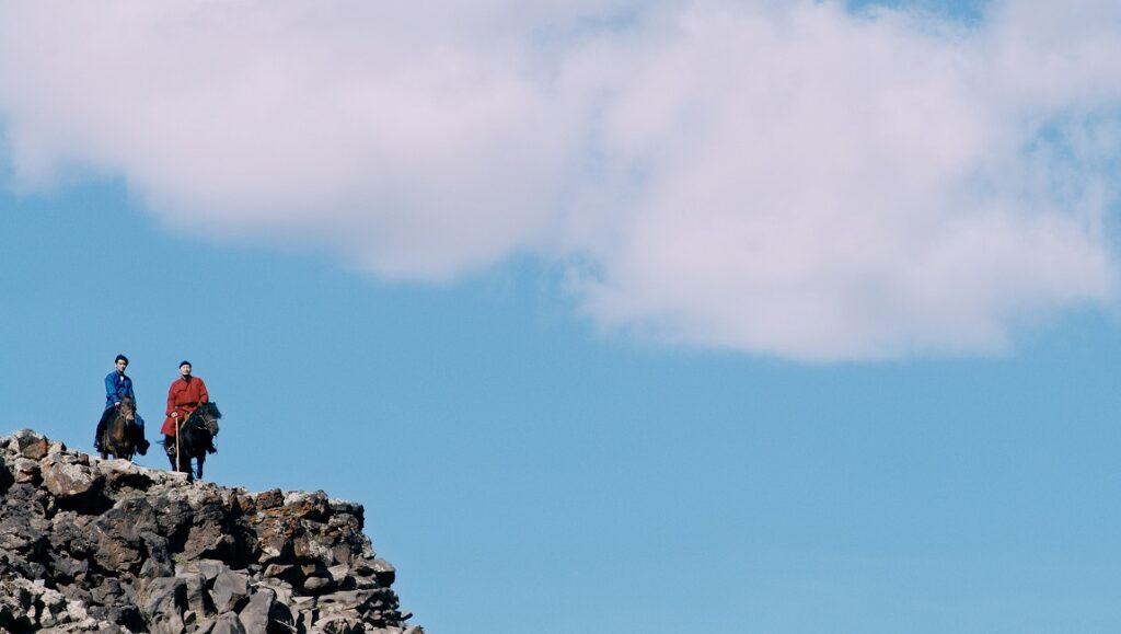 Two horse riders on a rocky cliff against a blue sky with clouds. Outdoor adventure, horseback riding.