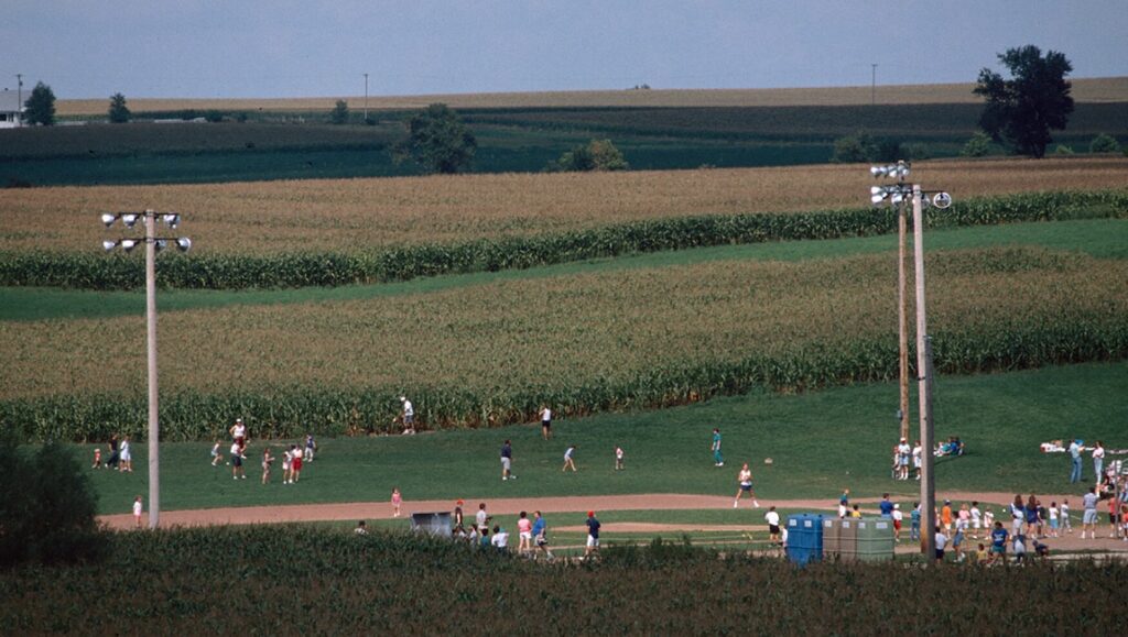 Still film: Baseball field with people playing, cornfields in background. James N. Kienitz Wilkins.