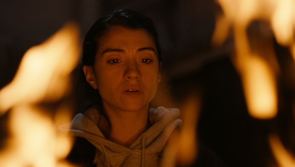 Ashkal: The Tunisian Investigation — Youssef Chebbi Ashkal: The Tunisian Investigation film still. Woman's face illuminated by fire. Youssef Chebbi film.