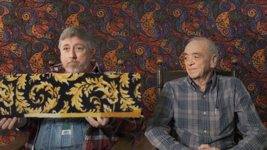 Carpet Cowboys: Noah Collier holds carpet with gold pattern. Emily MacKenzie sits beside him. Colorful patterned background.