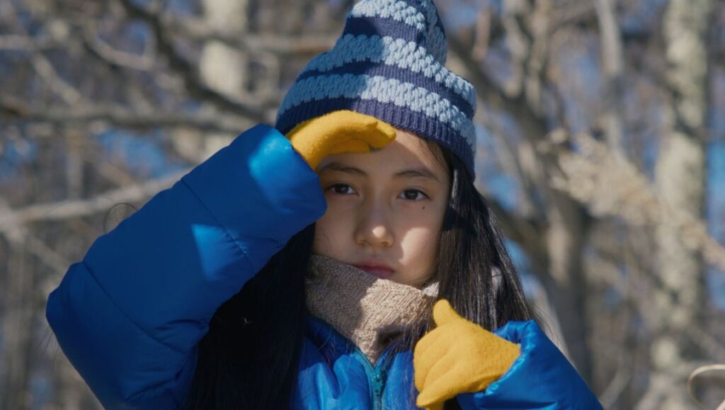 Hana Kino in Evil Does Not Exist, a Ryûsuke Hamaguchi film. Kino wears a blue hat and jacket, shielding her eyes.