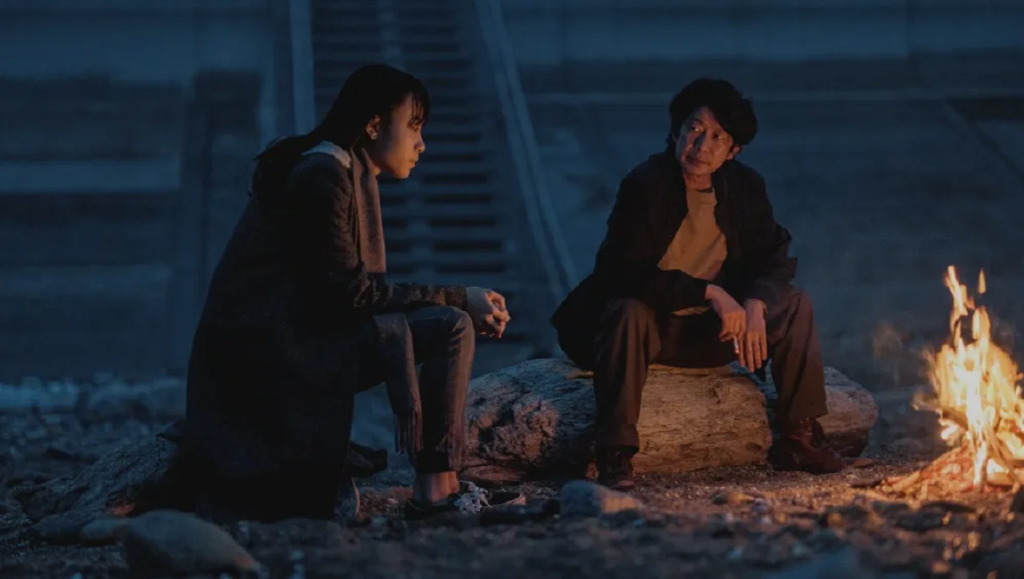 Last Shadow at First Light film still: Two figures sit by a campfire in a scene from the SGIFF '23 film.