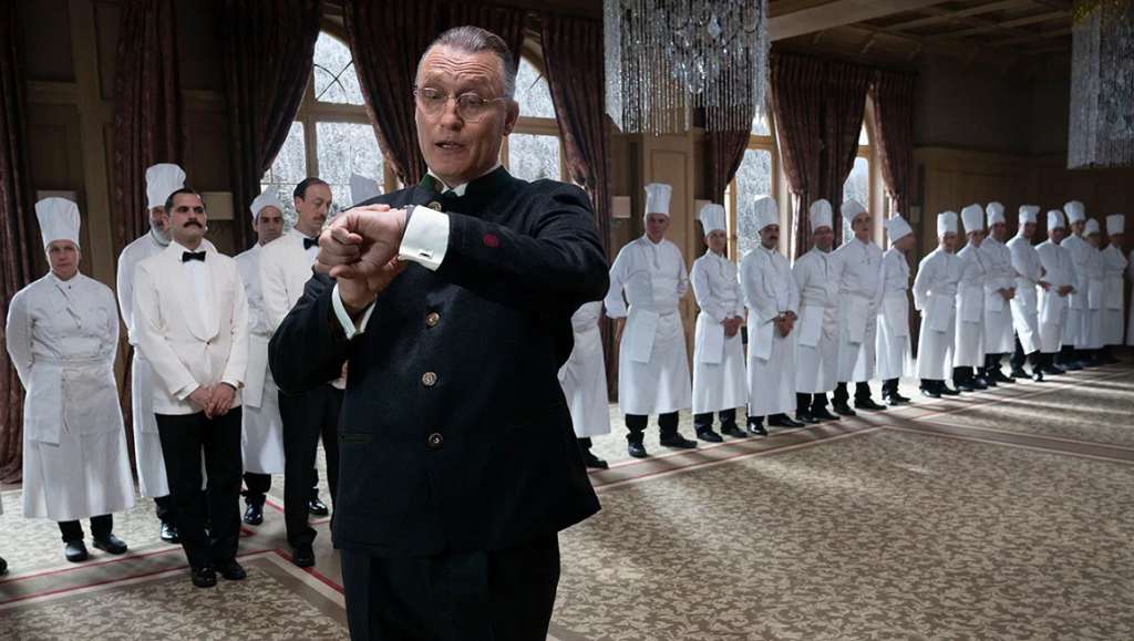 The Palace movie scene. Hotel manager checks watch, chefs line up. Venice '23 film review.