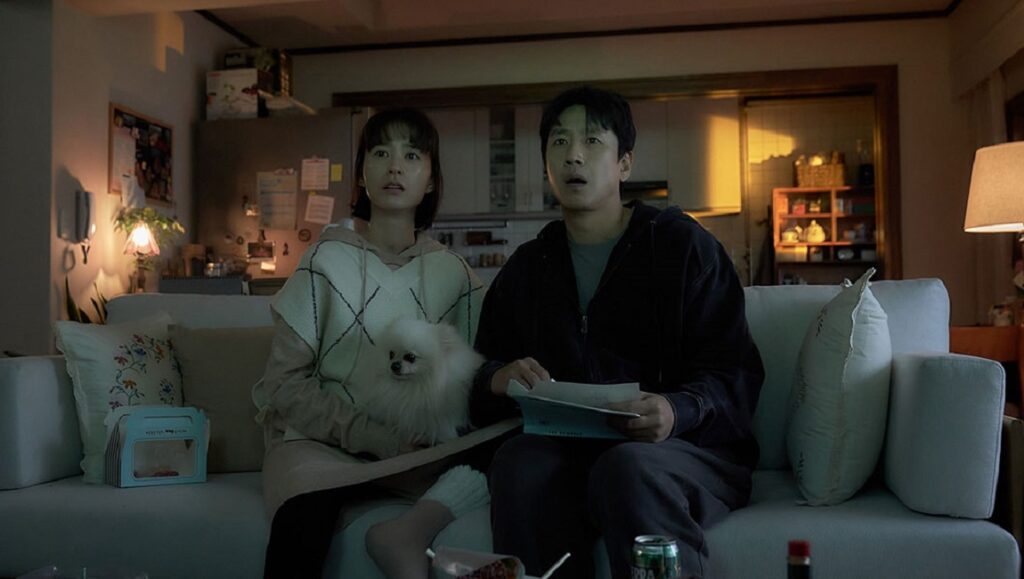 TIFF 2023 film Sleep scene. Couple, dog on couch, watching TV, startled. Dark, cozy living room.