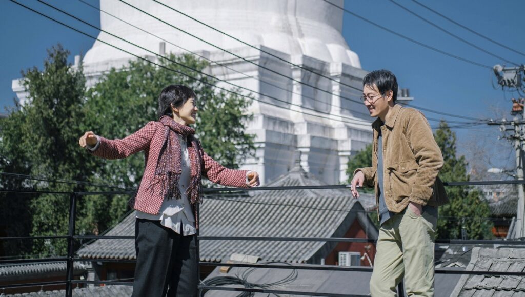 The Shadowless Tower at NYFF 2023. A woman and man stand on a rooftop with a white tower in the background.