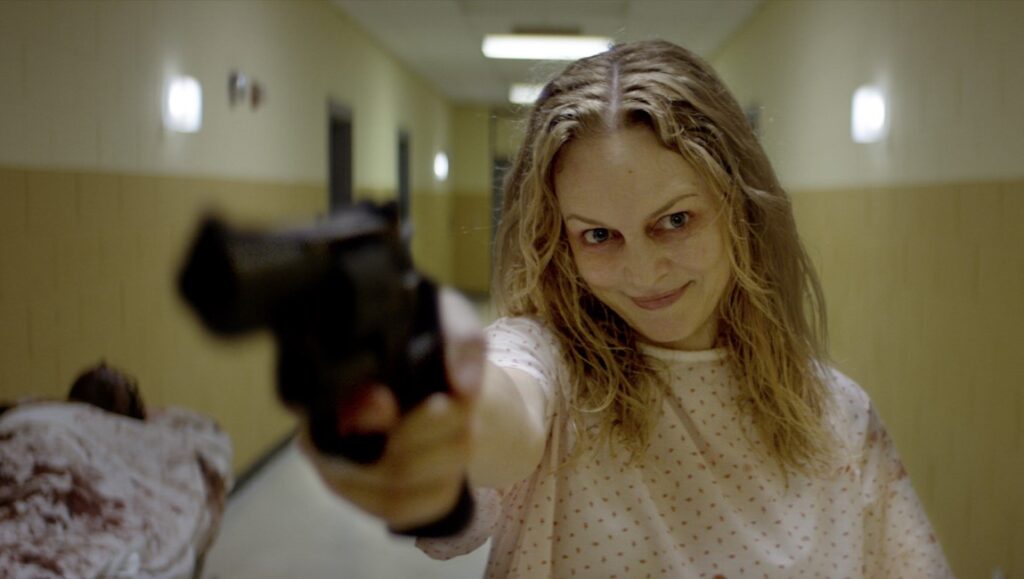 Suitable Flesh — Joe Lynch Still from *Suitable Flesh*: Woman in hospital gown points gun. Horror movie directed by Joe Lynch.