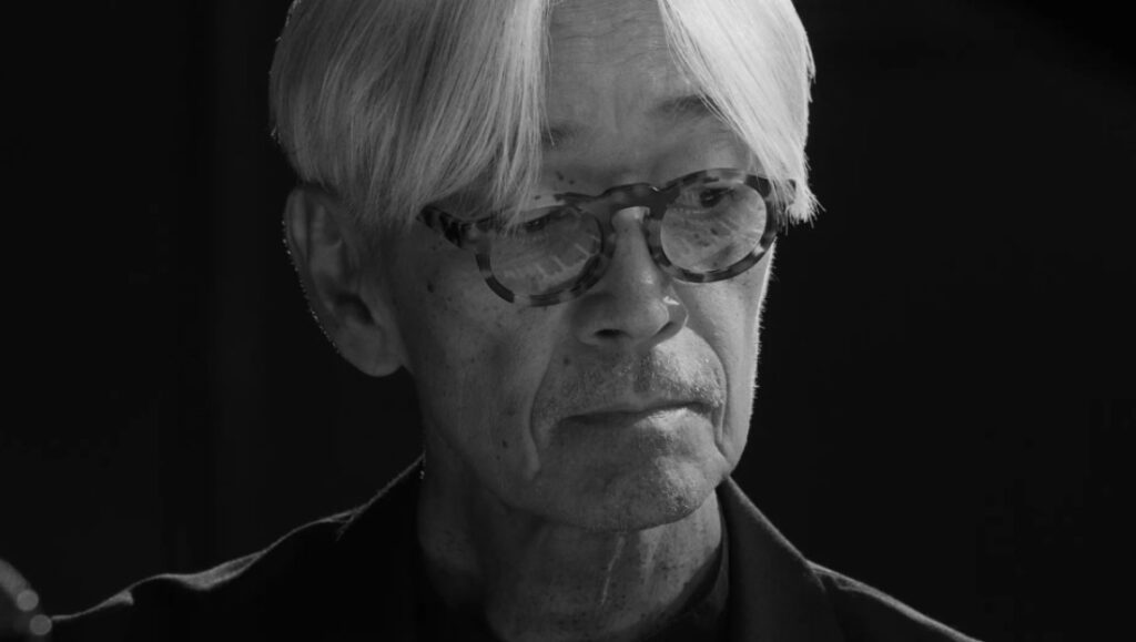 Black and white portrait of Ryuichi Sakamoto from Opus, a Neo Sora film. Sakamoto wears glasses.