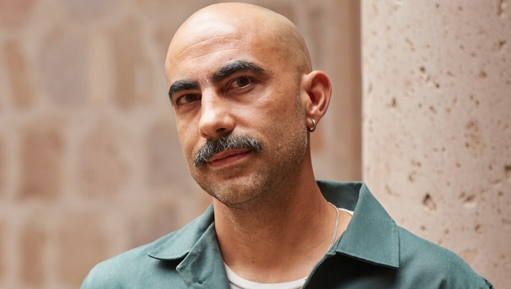 Fernando Frias, Mexican film director. Portrait from FICM23 interview. Bald man with mustache, wearing a green shirt.