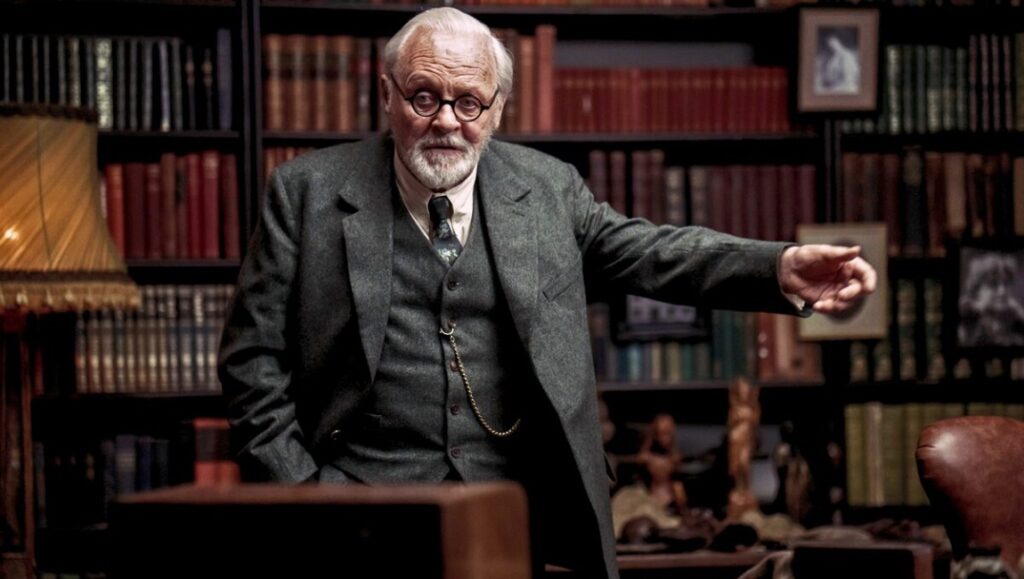 Anthony Hopkins as Sigmund Freud in Freud's Last Session movie. Freud stands in a library.
