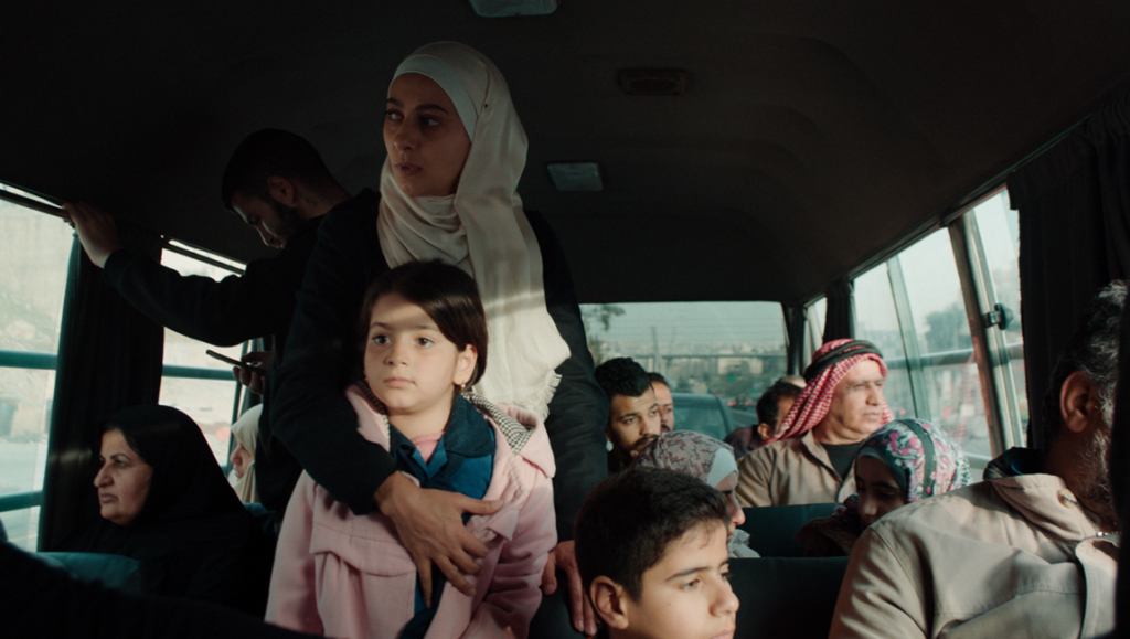 Scene from Inshallah A Boy movie. Woman in hijab with child on bus. Amjad Al-Rasheed film review.