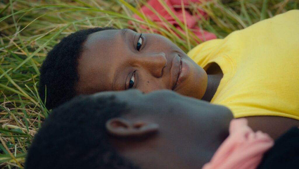 Banel & Adama film still. Two people lie in the grass, one wearing a yellow shirt. IFFR 2024 film.