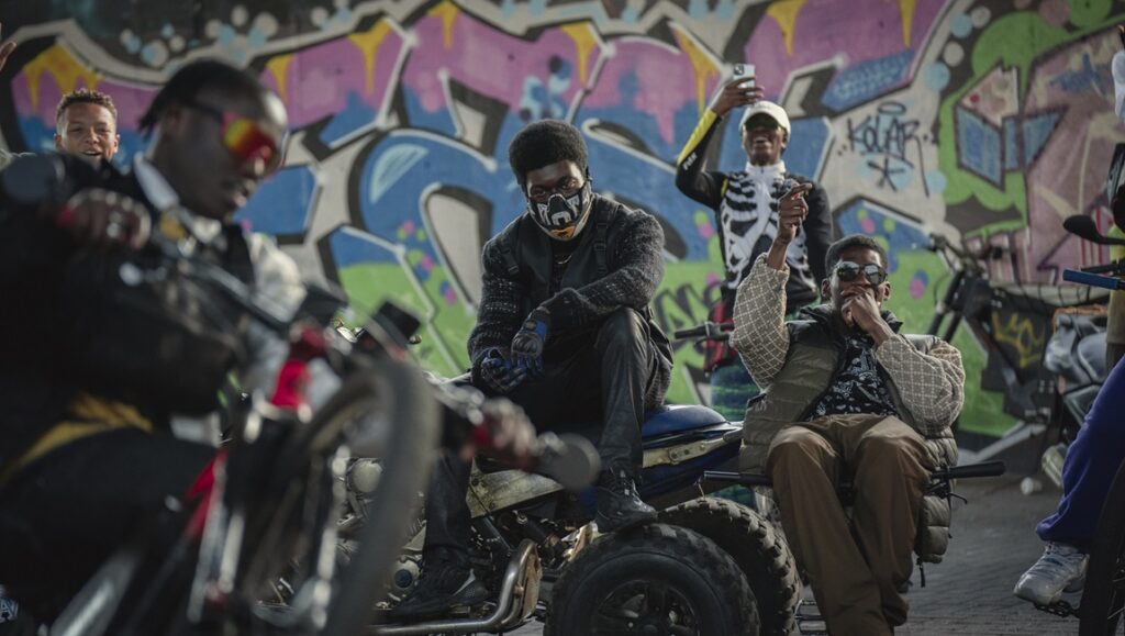 The Kitchen film review: Men on bikes pose in front of graffiti. Kibwe Tavares & Daniel Kaluuya film.