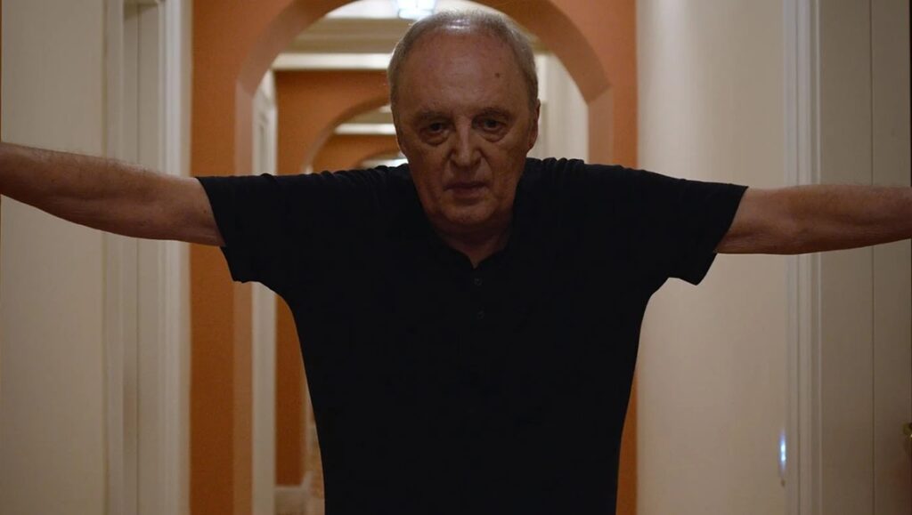 Dario Argento in Panico review. Italian filmmaker with arms outstretched in a hallway. Simone Scafidi film.