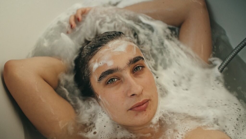 Apolonia in Lea Glob's Apolonia, Apolonia review. Woman in a bubble bath, looking at the camera.