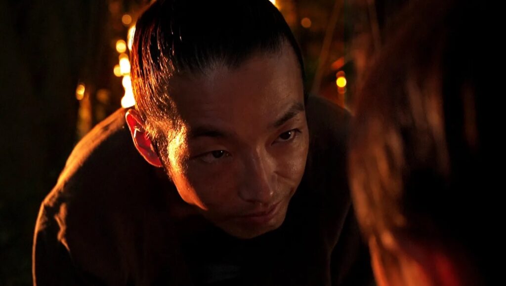IFFR 2024 film Shadow of Fire scene. Close-up of an Asian man looking downwards in warm lighting.