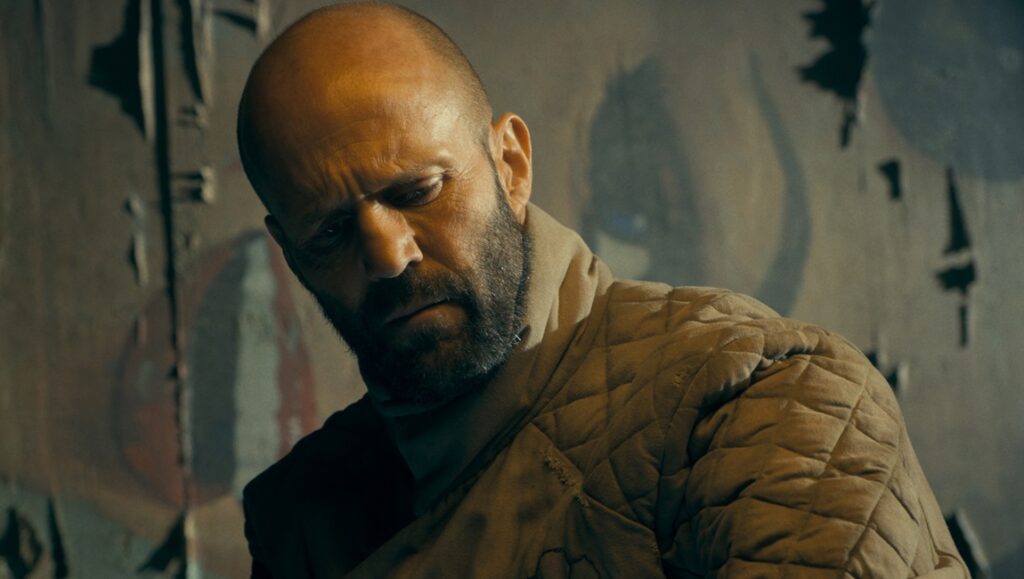 Jason Statham in The Beekeeper movie. Close-up of Statham with a beard, wearing a quilted jacket.