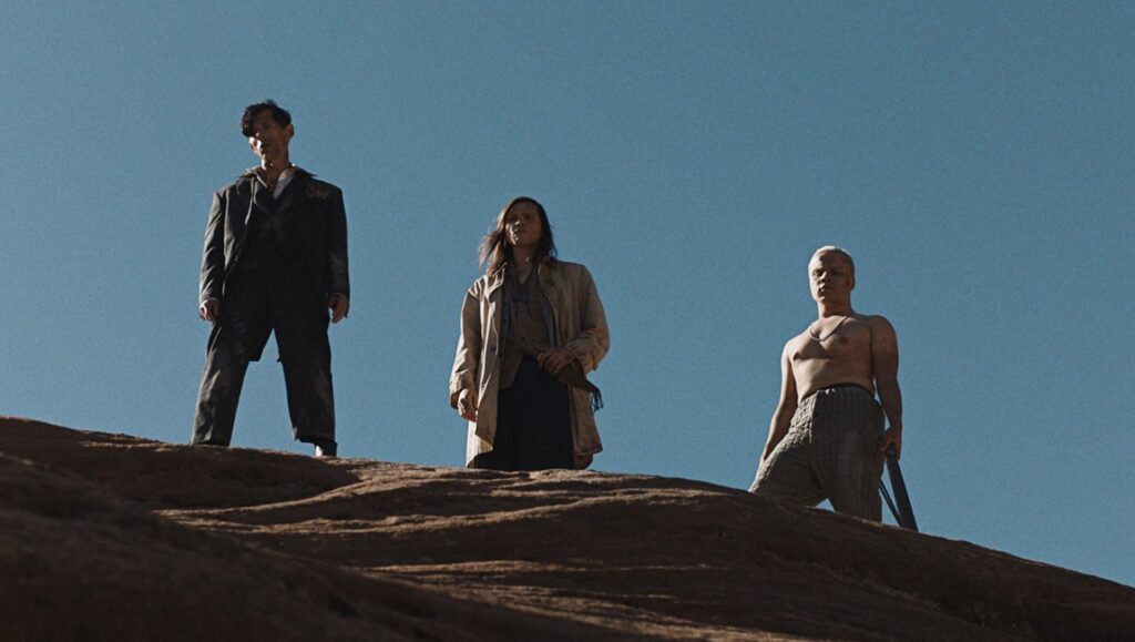 The Seeding movie image: Three figures on a desert hill under a blue sky. Barnaby Clay film review.