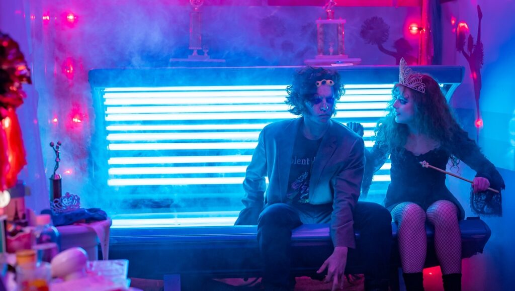 Lisa Frankenstein movie still. Kathryn Newton and Cole Sprouse in a scene with neon lights and a fantasy theme.