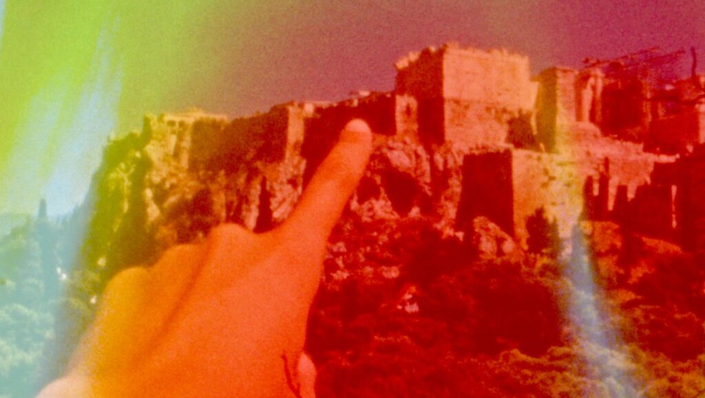 Deep Sleep by Basma al-Sharif: Finger points to ancient ruins in a dreamlike, color-washed landscape. Art film still.