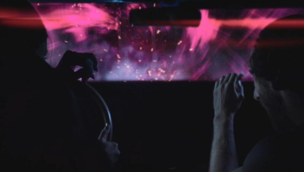Nevermore Film Festival: Hyperborean film scene. People in a car watch a pink, otherworldly event. Horror film.