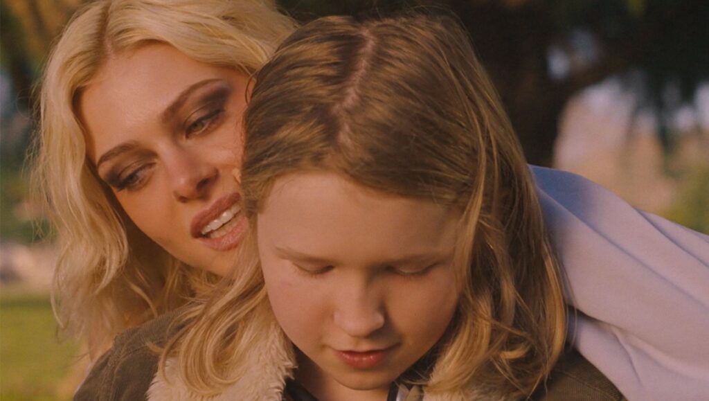 Nicola Peltz Beckham in Lola movie still. Blonde woman with heavy makeup next to a child with blonde hair.