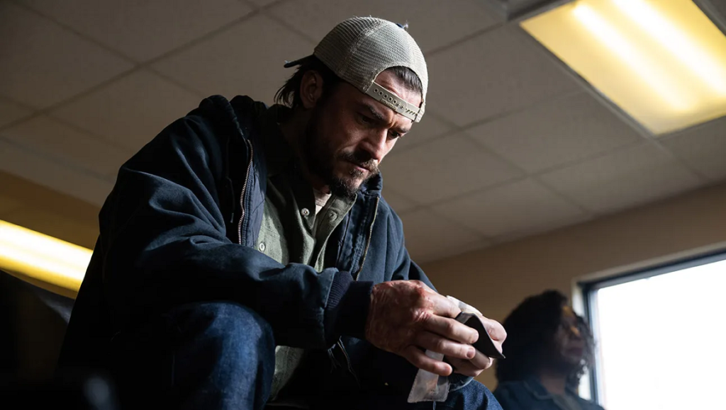 Still from Red Right Hand movie review. Man with a cap looking down, wrapping his injured hand.