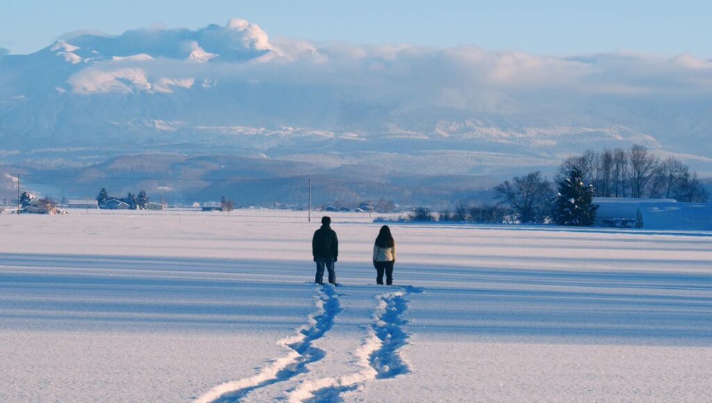 IFFR 2024 — Dispatch 2: Dear Kaita Ablaze, 13 Bombs, Elegies Couple walking in snowy field with mountain backdrop. Winter landscape with footprints.